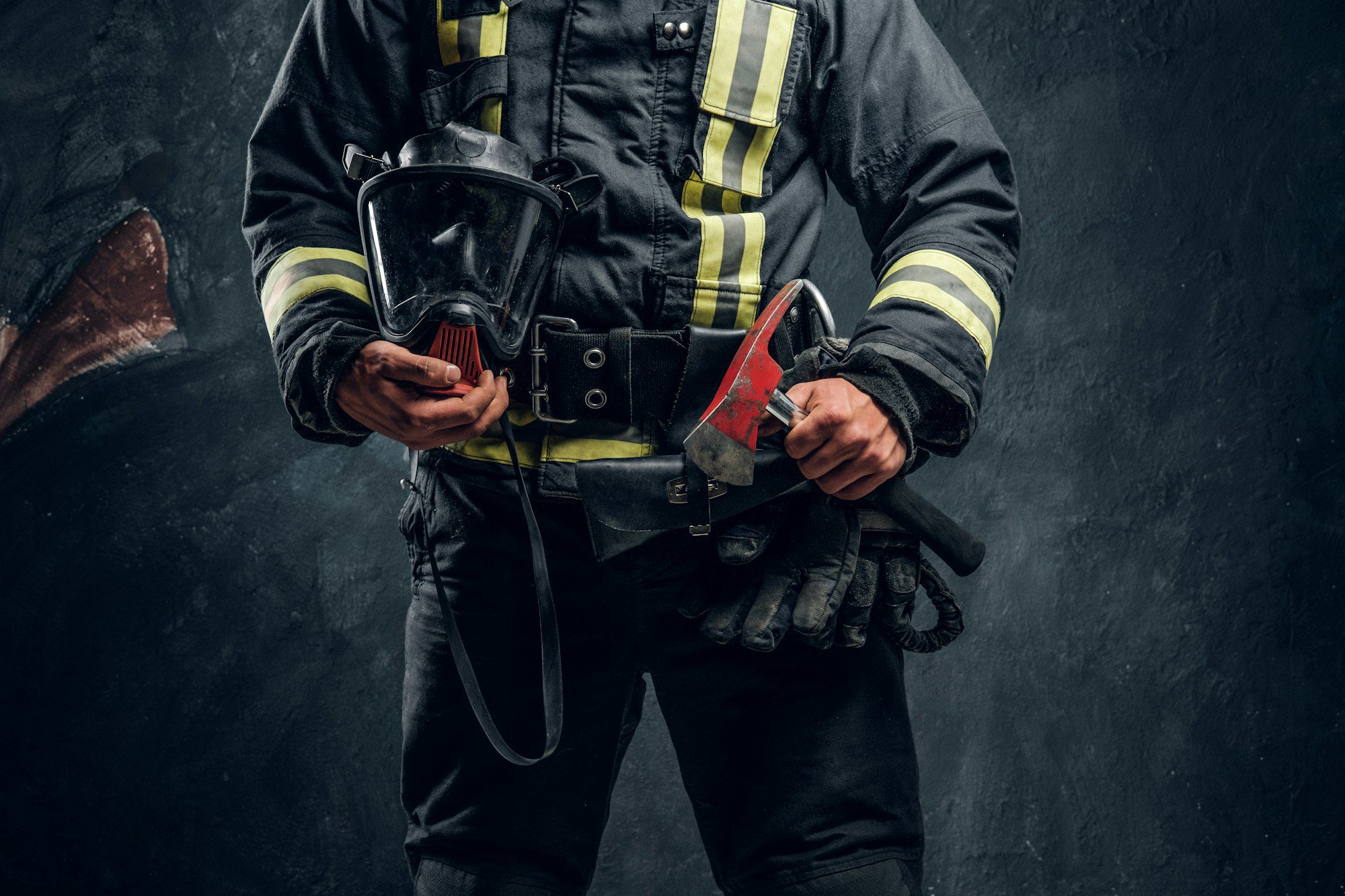 Firefighter in protective gear holding a chainsaw and mask, symbolizing emergency response and dedication to safety.