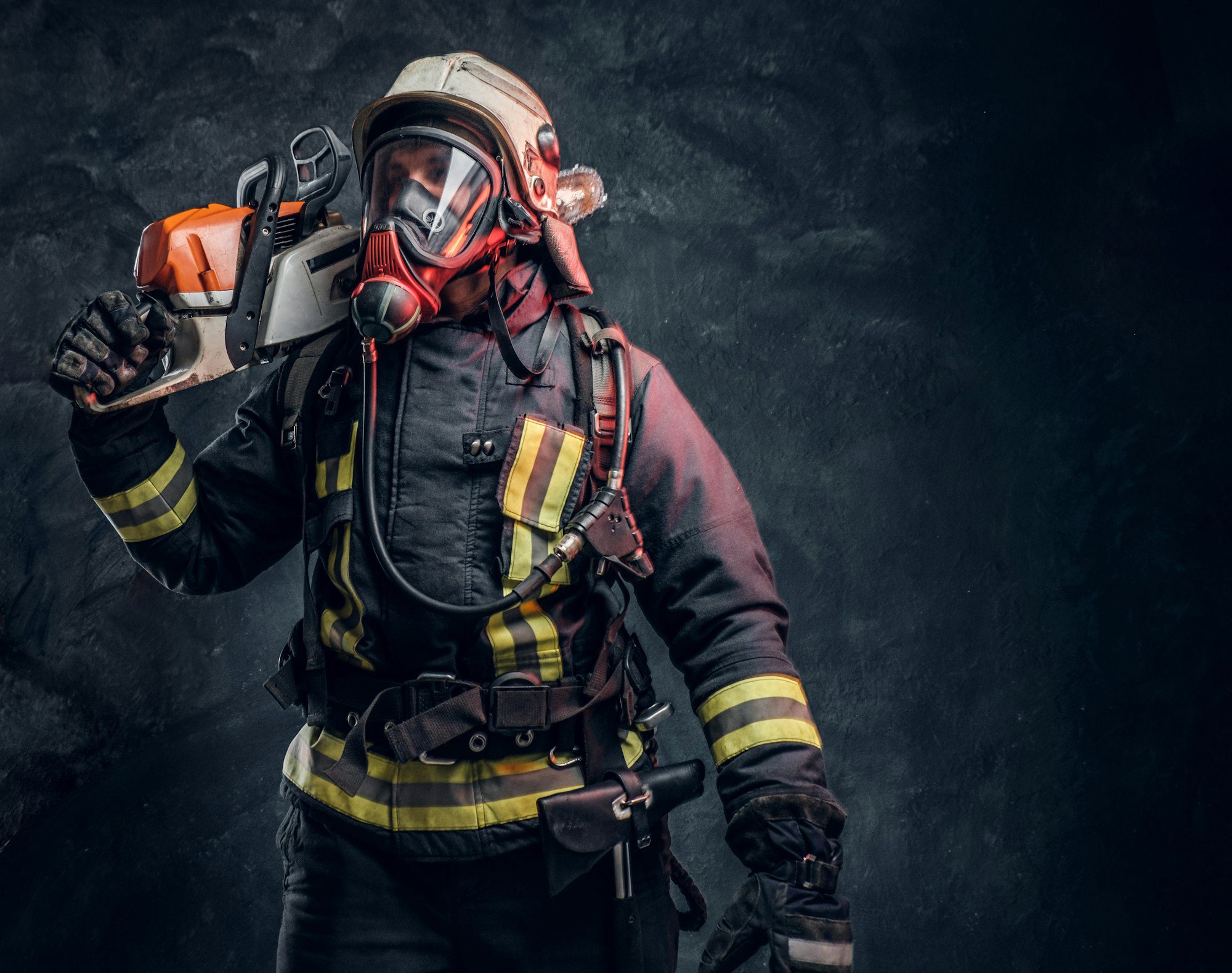 Firefighter in safety helmet and oxygen mask holding chainsaw, representing emergency response and dedication to safety.